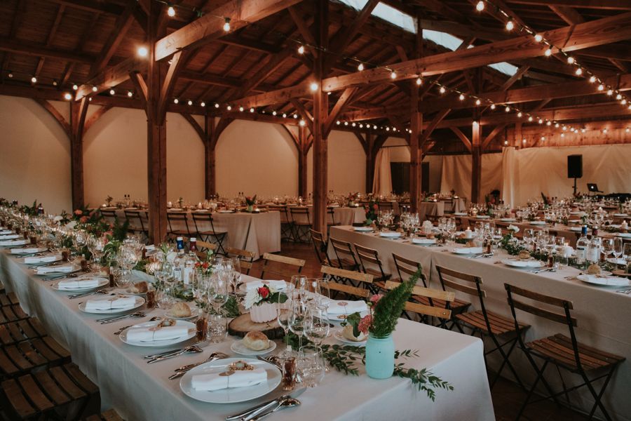 Grange de mariage avec une décoration rustique et champêtre aux petits vases de fleurs sur des tables rectangulaires.