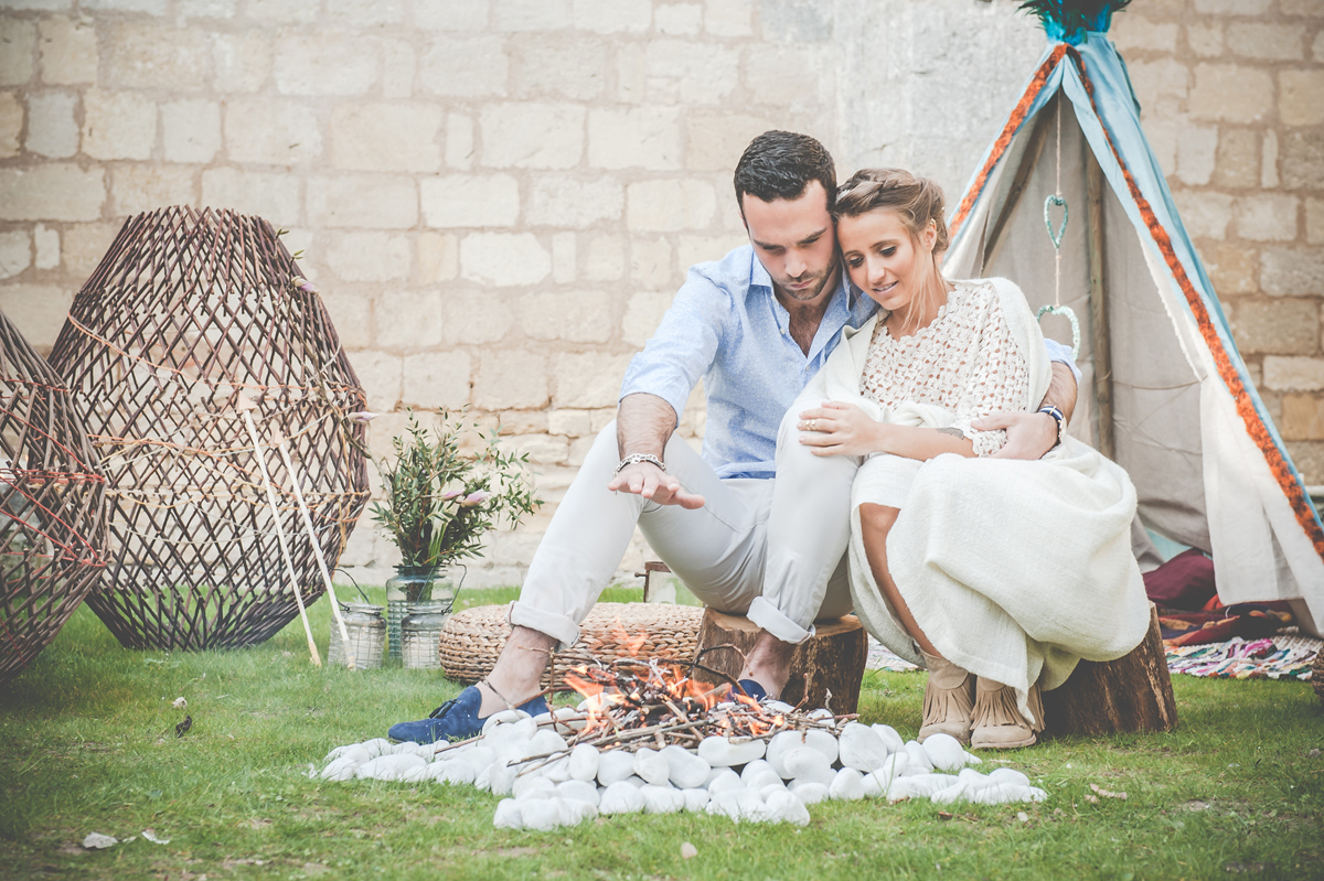 Décoration de mariage en extérieur au thème bohème romantique avec banc en bois, tipi et feu de déco.