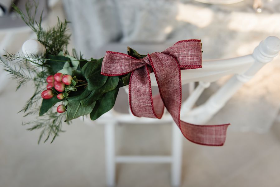 Décoration de chaise de mariage en novembre en ruban rouge et feuillage vert.