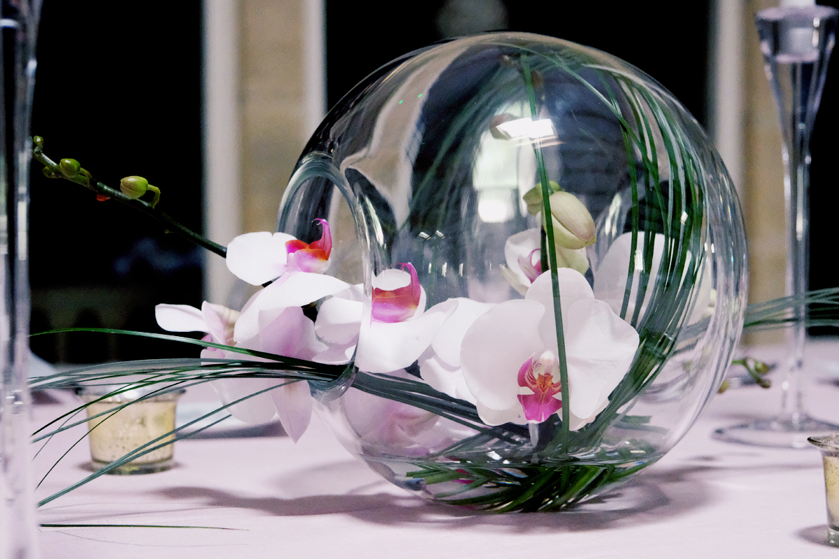 Un bouquet dans un vase rond, composé de flexiglass et d'orchidées.