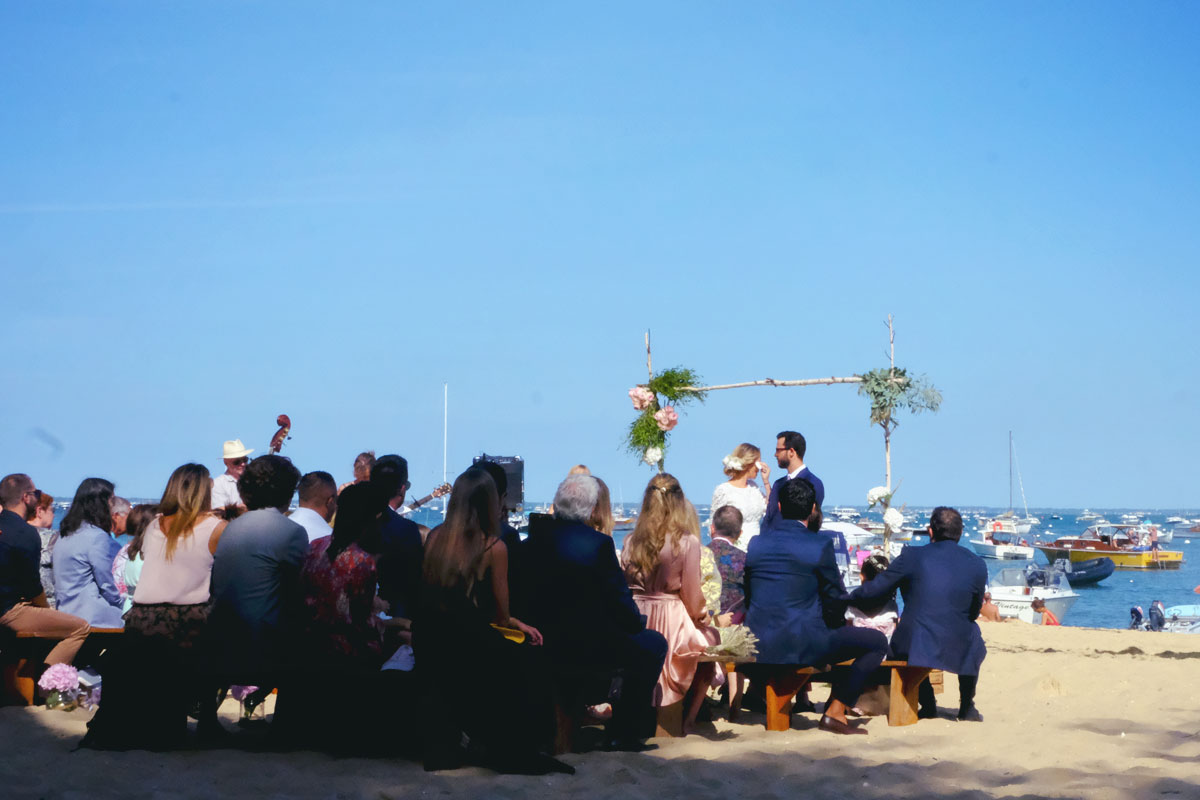 Les mariés sous leur arche de mariage bohème chic en bord de mer sur le sable de la plage d'Aquitaine.